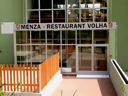 Vchod do menzy: prosklená stěna s nápisem Menza – Restaurant Volha, vlevo oranžový dřevěný plůtek